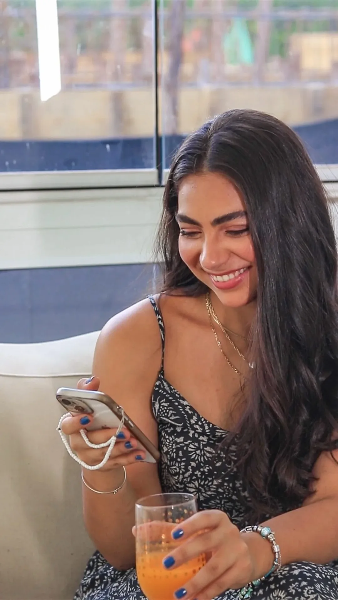 Rebeca Campano sorrindo para o celular, com um copo de suco na mão