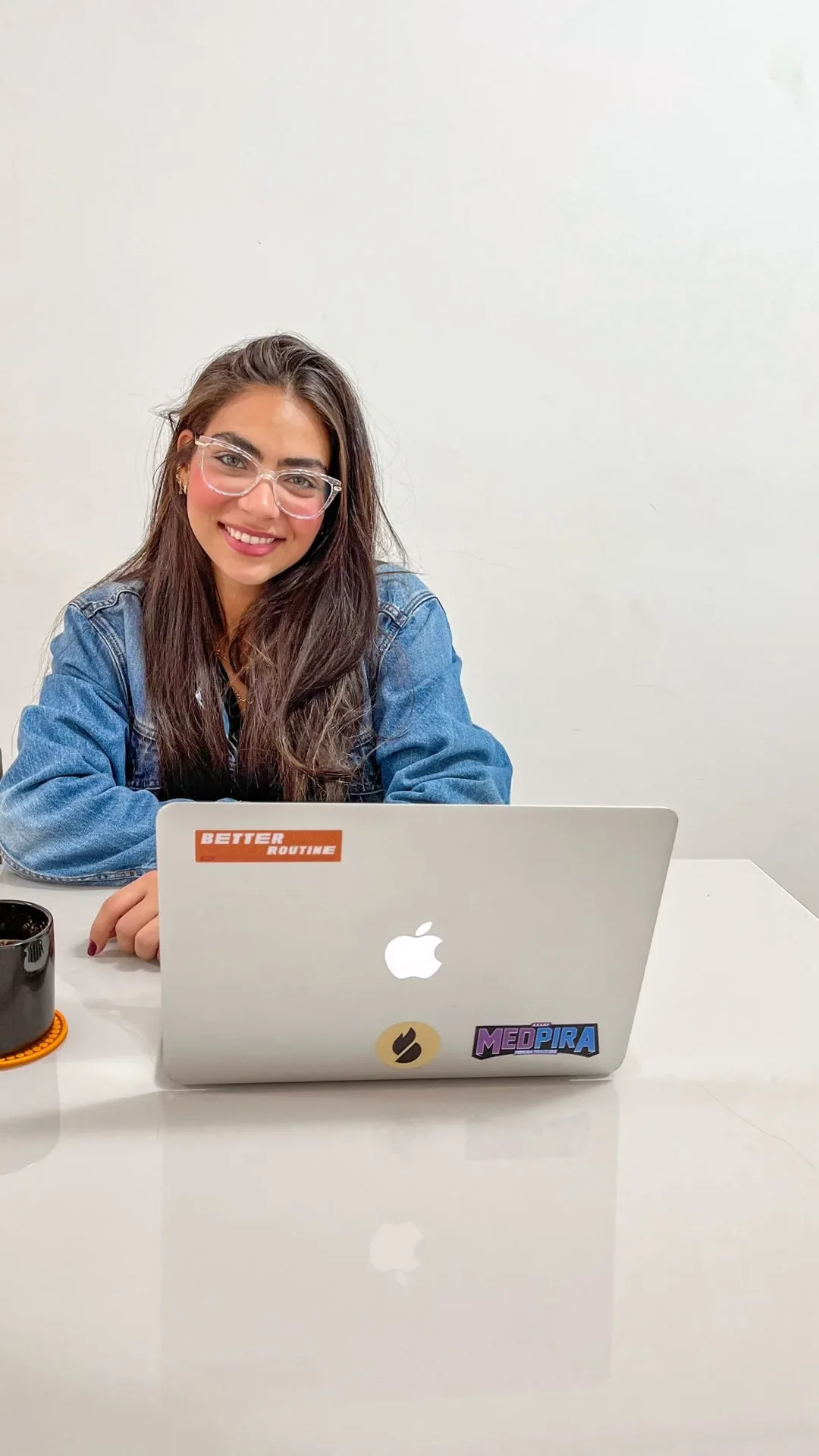 Rebeca Campano sorrindo diante de um notebook, de óculos e jaqueta jeans