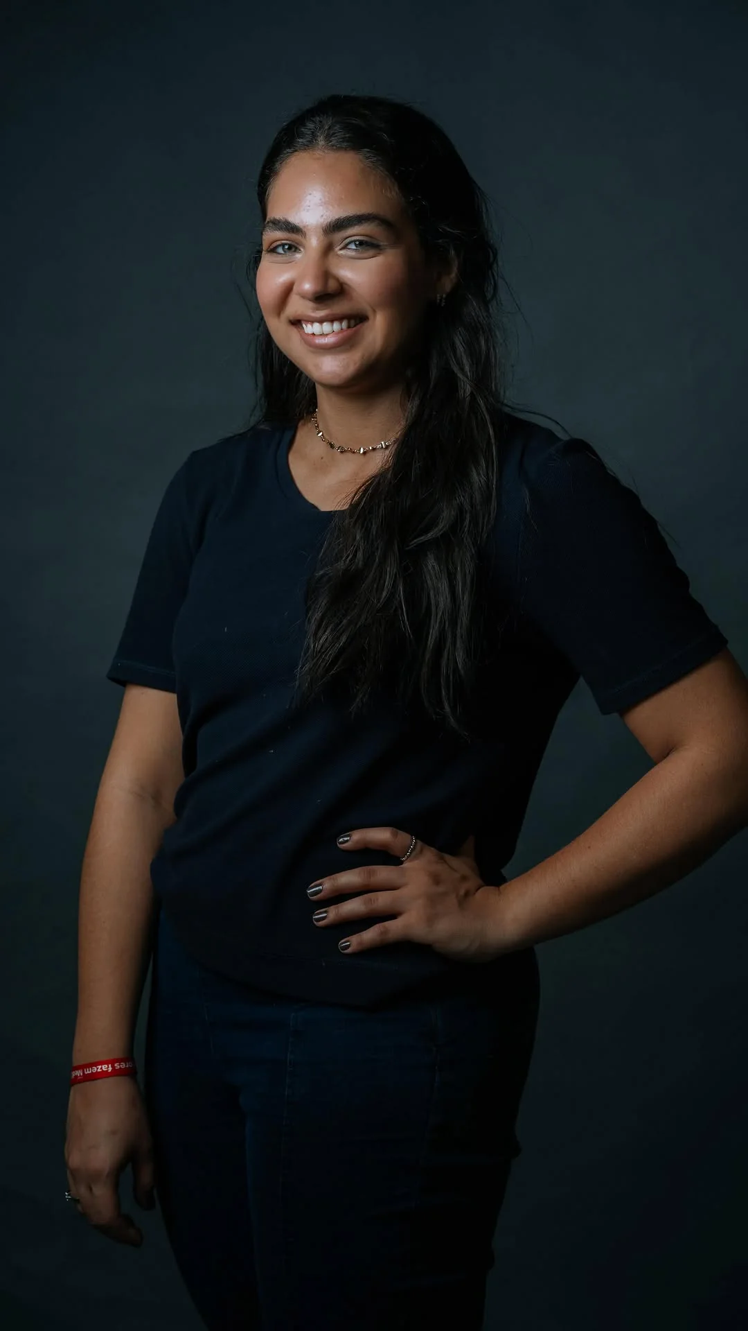 Rebeca Campano em retrato de estúdio com fundo escuro, sorrindo de braços na cintura